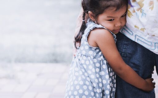 Sad little girl hugging her mother's leg